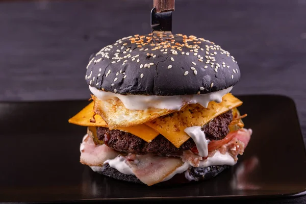 Hamburger  with bacon and fried eggs in black roll with sesame