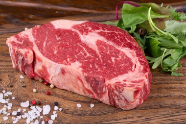 Çiğ et, yeşillikli ahşap bir tahtanın üzerinde baharatlı Ribai bifteği.