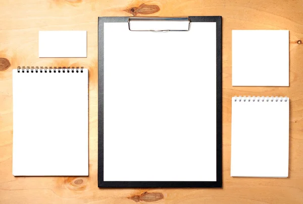 Blank clipboard, business card and notepads on wooden background. Business essentials.