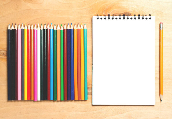 Business essentials. Top view of spiral blank notebook and color pensils on wood desk background