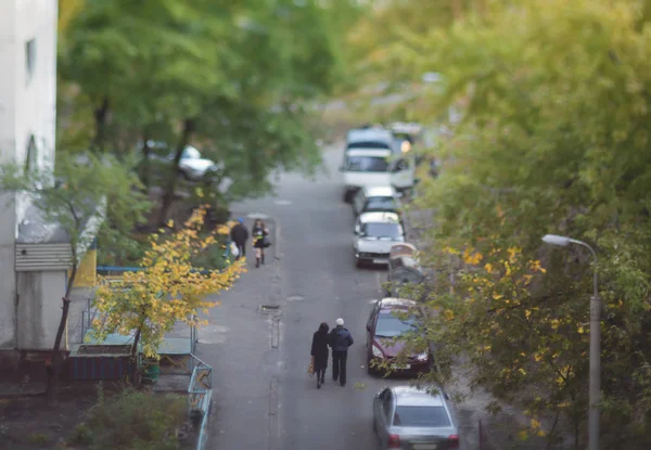 Couple walks in the yard of an apartment house. Blurry tilt-shift cityscape.