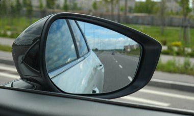 Arabanın dikiz aynasına demir parmaklıkları olan boş bir otoyol yansıtılır. 