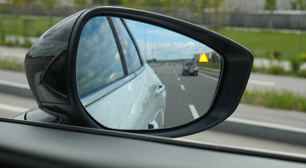  A pictogram signaling the approach of a car from behind in the mirror of a car on a multi lane highway