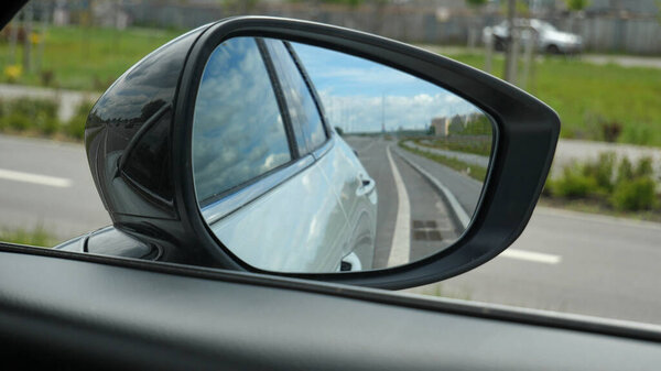 A view of the roadside of a modern highway in the side mirror of a standing car ready to drive