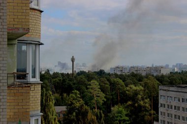 Çok katlı bir binanın balkonundan gökyüzüne yükselen dumanlı bir şehirde yangın manzarası.