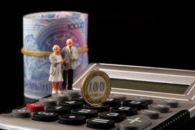 10,000 tenge banknot, 100 tenge sikke, bir hesap makinesi ve emekli heykelcikleriyle Kazakistan 'daki emekli aylıkları hakkında kavramsal plan