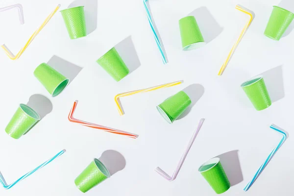 Flat lay pattern decoration of disposable cups and straws. Overhead view composition of summer party utensils of vivid colours on white background with hard shadows.