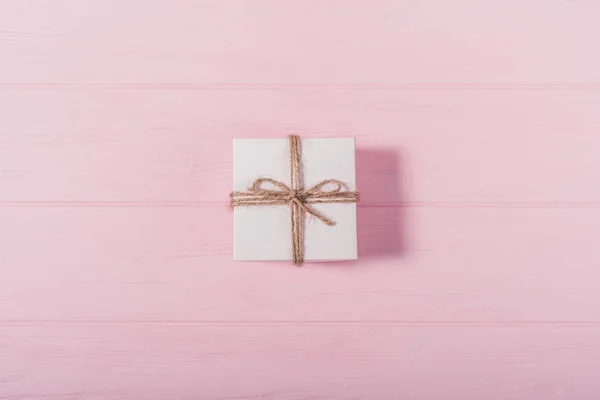 Small white gift box tied with rope on pink wooden background, top view. Flat lay minimal composition with copy space.