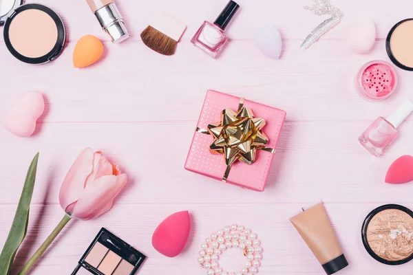 Gift box among beauty products on pink table