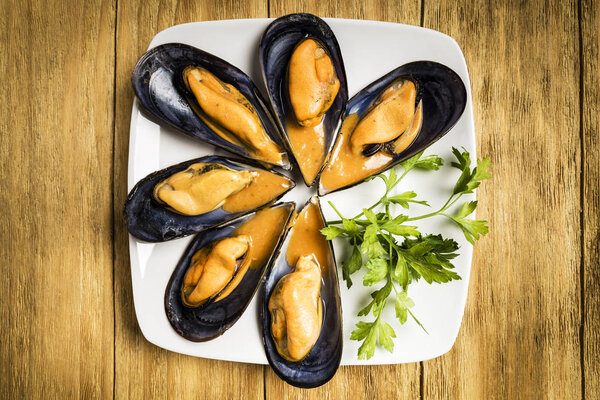 Cooked mussels with parsley and orange sauce and half a lemon on a white plate on a wooden table