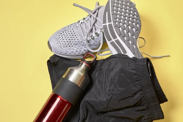 Running shoes with a pair of shorts and a water bottle on a yellow background