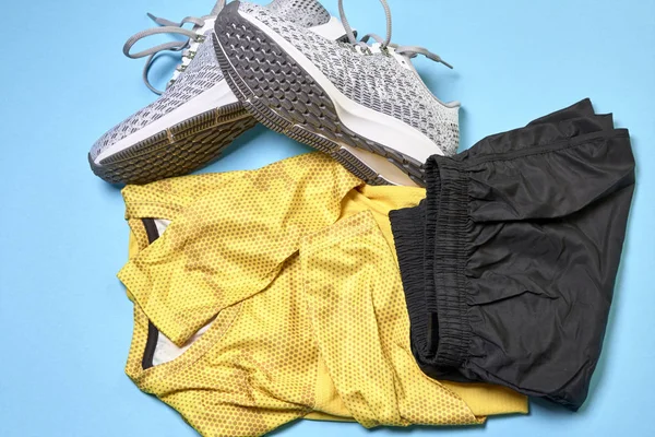 running shoes next to a shorts and a yellow shirt on a blue background