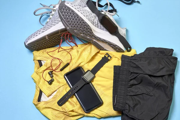 running shoes with a pair of shorts, a yellow shirt and technological accessories on a blue background