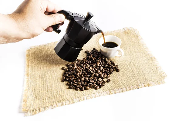 Hombre sirviendo una taza de café con una cafetera italiana al lado de una pila de granos de café — Foto de Stock