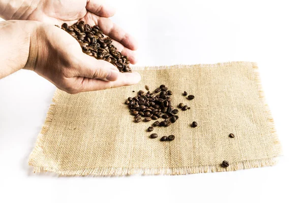 Manos de hombre dejando caer un montón de granos de café en un mantel de tela de rafia — Foto de Stock