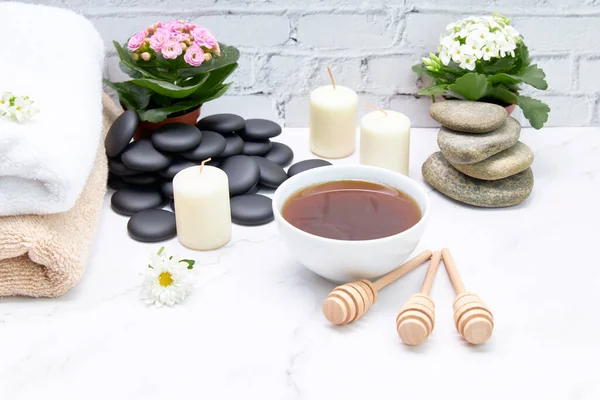 Honey in a bowl with some towels and some flowers on a marble table. Skin care and beauty treatment concept