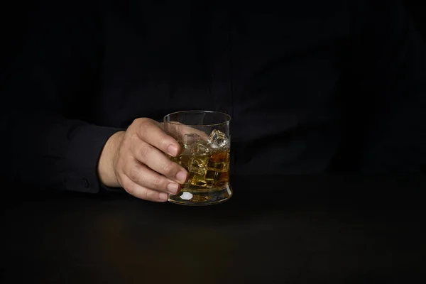 close-up of a man\'s hands with a glass of Scotch and ice on a dark background. Concept of social problems