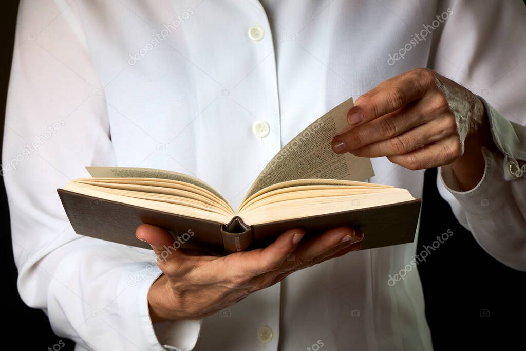 Person reading a book on a dark background. Concept education, hobby.
