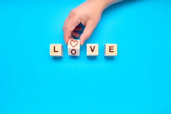 Person placing the word LOVE in wooden squares on a blue background with space for copying. The heart as a symbol of love