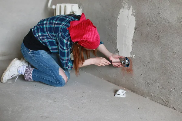 La chica está haciendo reparaciones en el apartamento. Casa mudándose a un nuevo apartamento. El trabajador hace reparaciones, enlucido y taladra la pared . — Foto de Stock