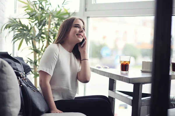 Ung flicka på ett café. Flickan sitter i soffan och pratar i telefon. — Stockfoto