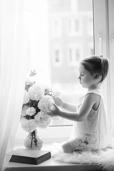 Una niña está sentada en el alféizar de la ventana. Un ramo de flores —  Fotos de Stock