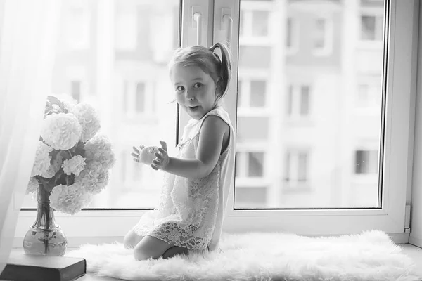 A little girl is sitting on the windowsill. A bouquet of flowers — Stock Photo, Image