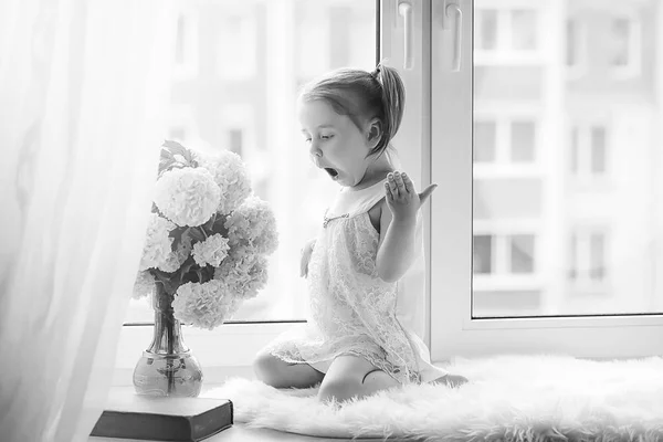 Una niña está sentada en el alféizar de la ventana. Un ramo de flores —  Fotos de Stock