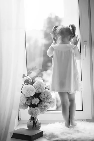 Une petite fille est assise sur le rebord de la fenêtre. Un bouquet de fleurs — Photo