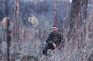 Kamuflaj ve bir sp üzerinde bir ormanda bir av tüfeği ile bir adam