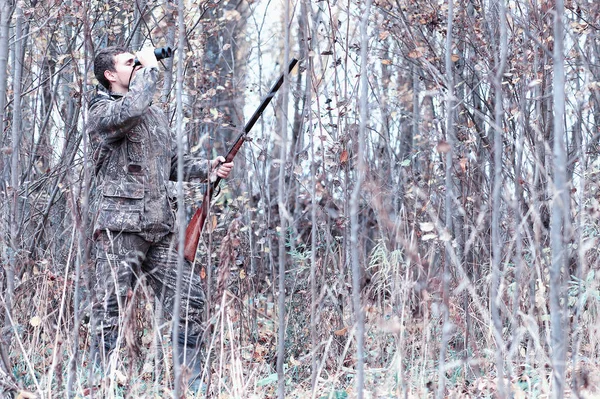 Un hombre en camuflaje y con un rifle de caza en un bosque en una sp — Foto de Stock