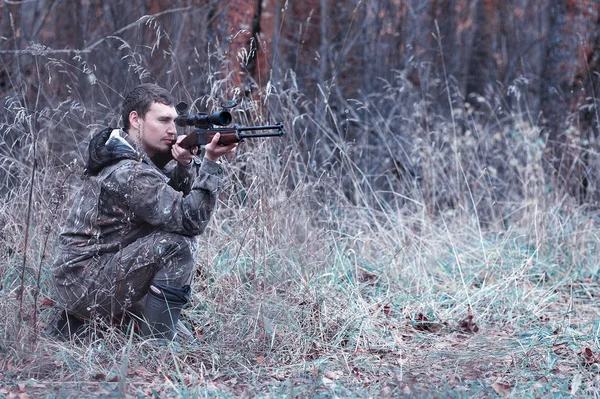 Um homem em camuflagem e com uma espingarda de caça em uma floresta em uma sp — Fotografia de Stock