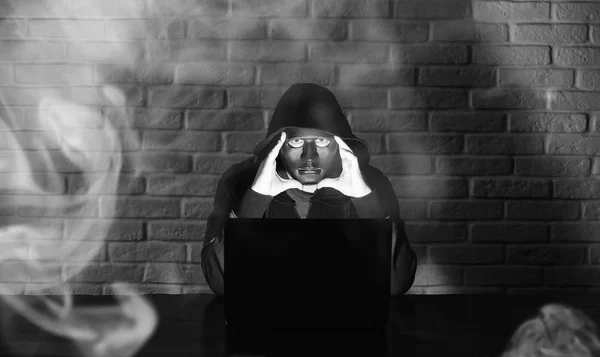 Hacker in black mask and hood at the table — Stock Photo, Image