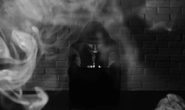 Hacker in black mask and hood at the table — Stock Photo, Image