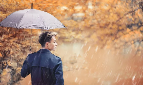 Herbstliches Regenwetter und ein junger Mann mit Regenschirm — Stockfoto