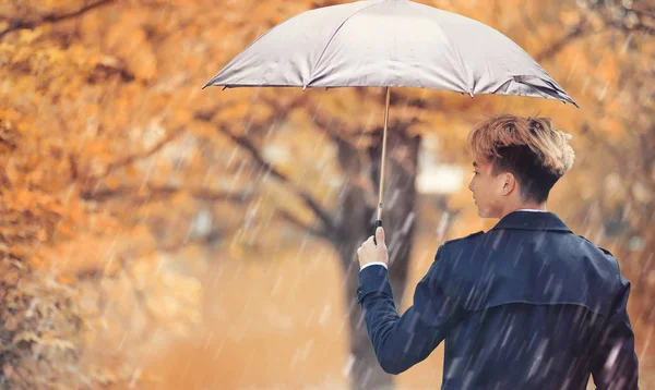 Herbstliches Regenwetter und ein junger Mann mit Regenschirm — Stockfoto