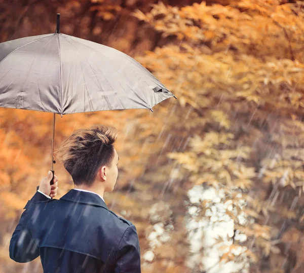 Autunno tempo piovoso e un giovane uomo con un ombrello — Foto Stock