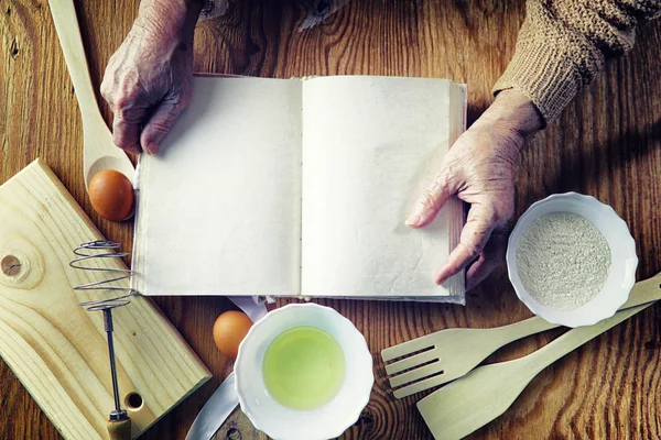 Open recipe book in the hands of an elderly woman — Stock Photo, Image