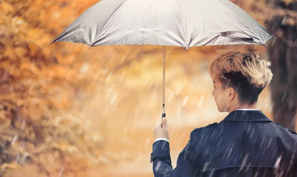 Herbstliches Regenwetter und ein junger Mann mit Regenschirm — Stockfoto