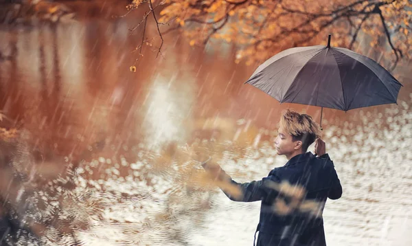 Autunno tempo piovoso e un giovane uomo con un ombrello — Foto Stock