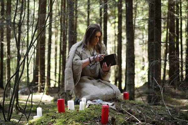 Um homem numa batina passa um ritual numa floresta escura. — Fotografia de Stock