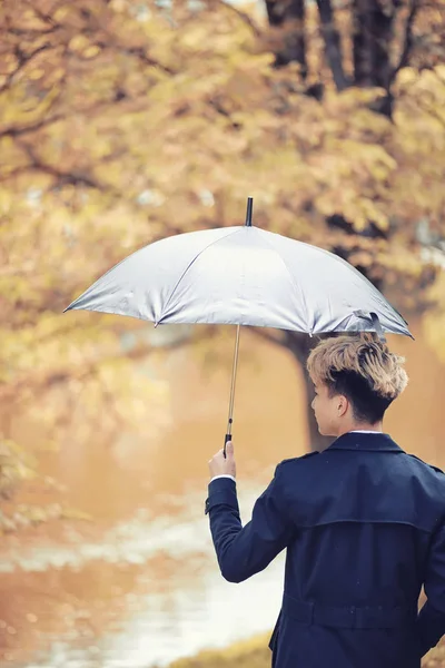 Herbstliches Regenwetter und ein junger Mann mit Regenschirm — Stockfoto