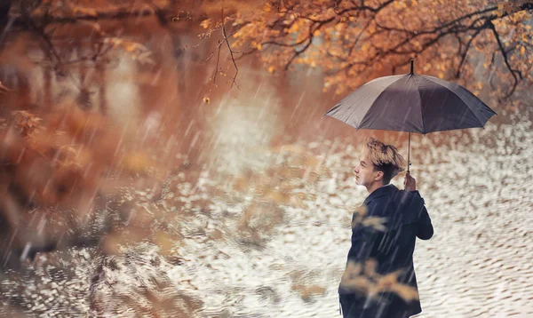 Sonbahar yağmurlu hava ve bir şemsiye ile genç bir adam — Stok fotoğraf