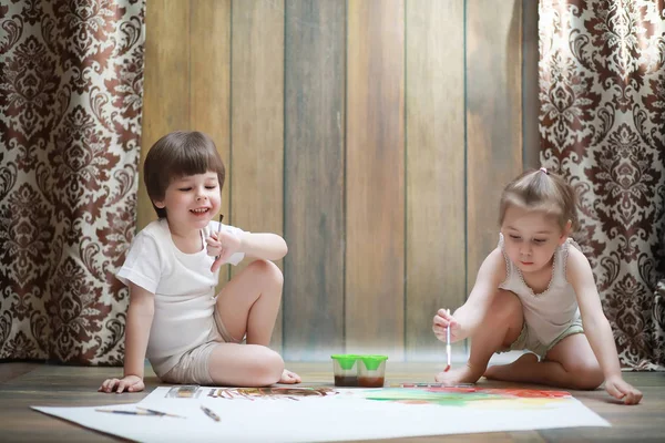 Niños pequeños pintan en una hoja grande de papel —  Fotos de Stock