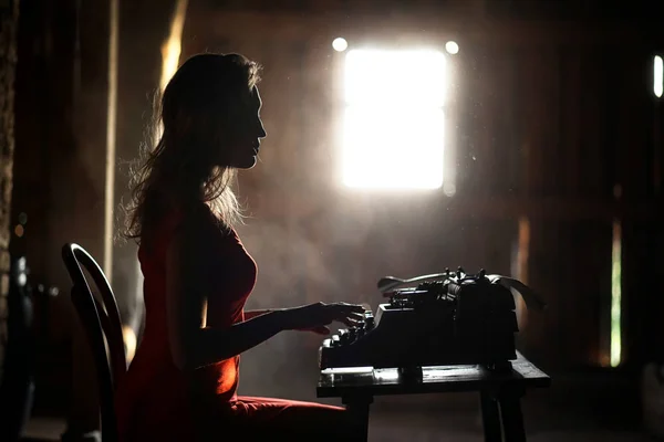 Uma menina no estilo retro imprime em uma máquina de escrever velha — Fotografia de Stock