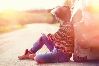 Adam yolda arabanın yanında oturuyor