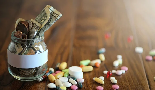 Drogy a mince ve skleněné nádobce na dřevěné podlaze. Kapesní úspory — Stock fotografie