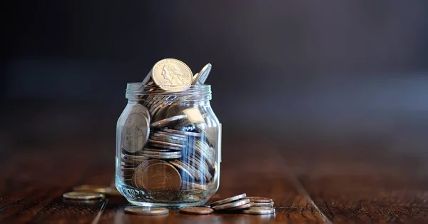 Monedas en un frasco de vidrio en un suelo de madera. Ahorro de bolsillo de la moneda —  Fotos de Stock