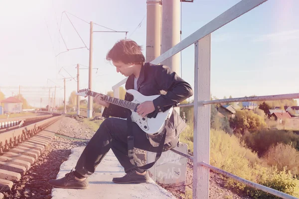 A man with an electric guitar on the railway. A musician in a le — Stock Photo, Image