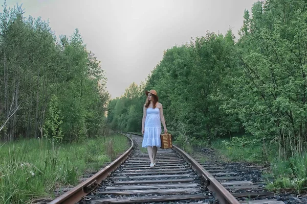 Дівчина в білому сараї і плетеній валізі, що ходить на рейках — стокове фото
